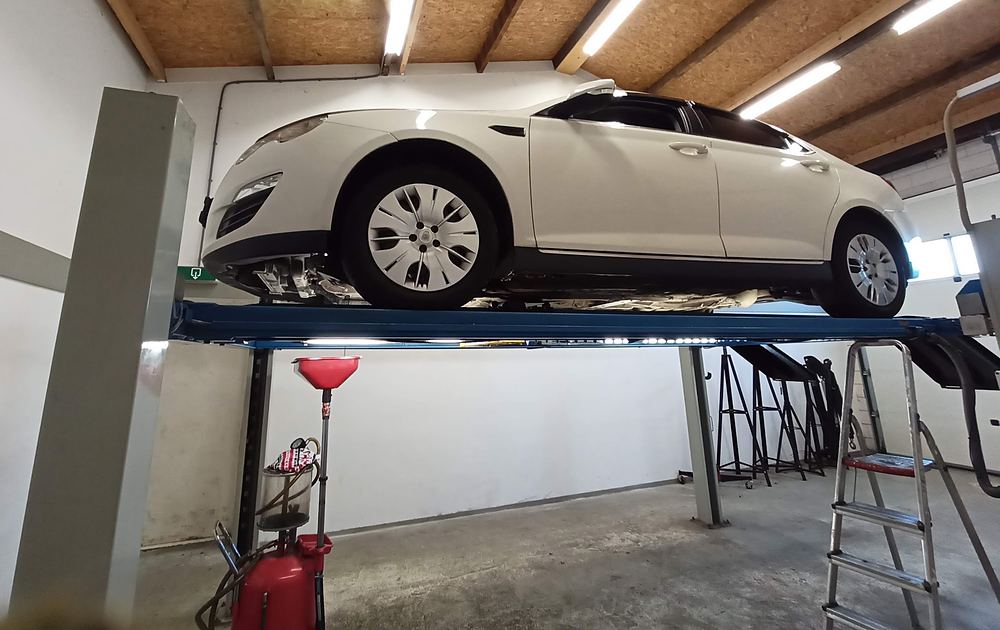 Een witte auto hoog op de brug, met opvangbak en trap eronder