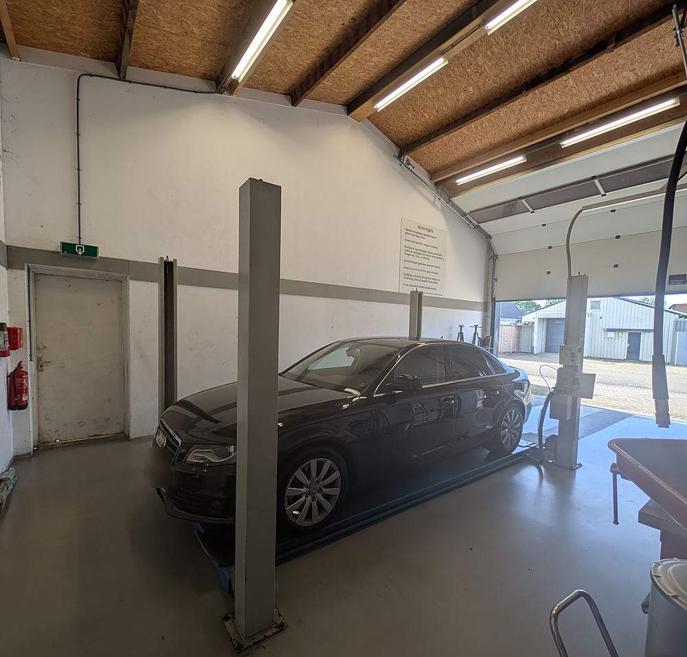 De werkplaats met de roldeur open en een auto naast de brug